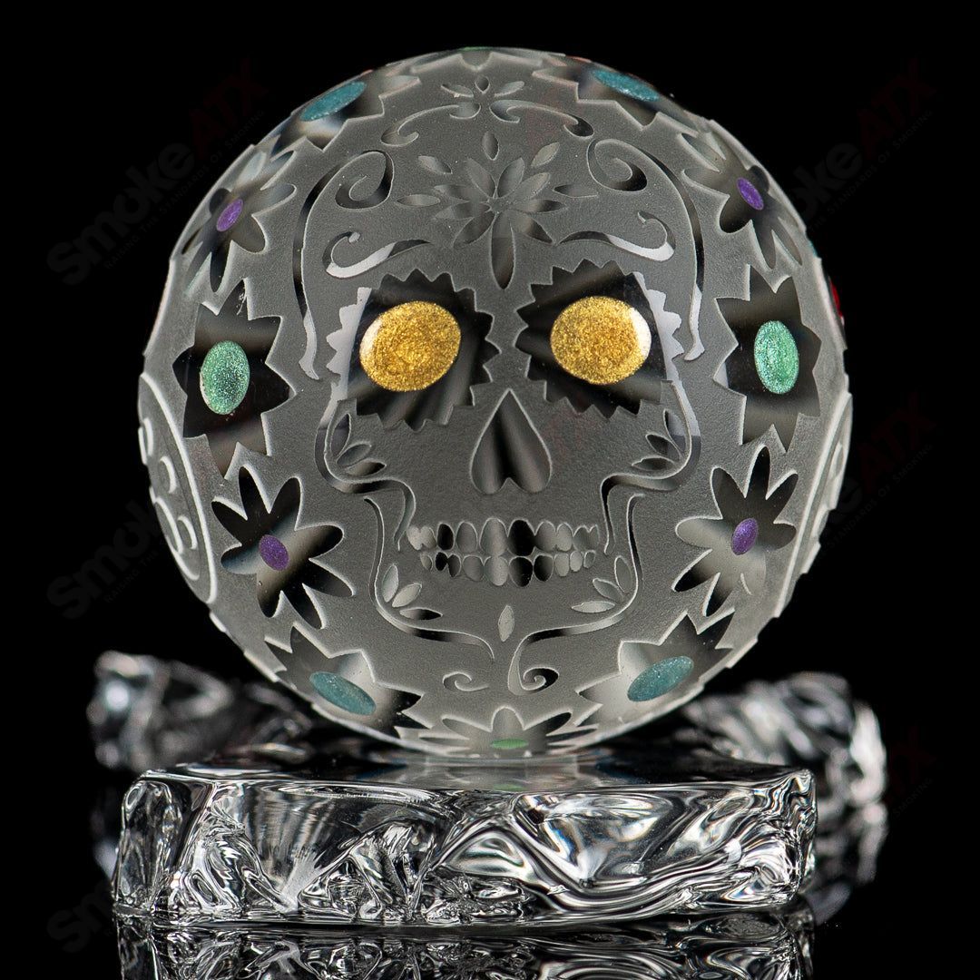 Faceted skull marble by Fatal Facets, made of glass with intricate faceted design, resting on a neutral surface.