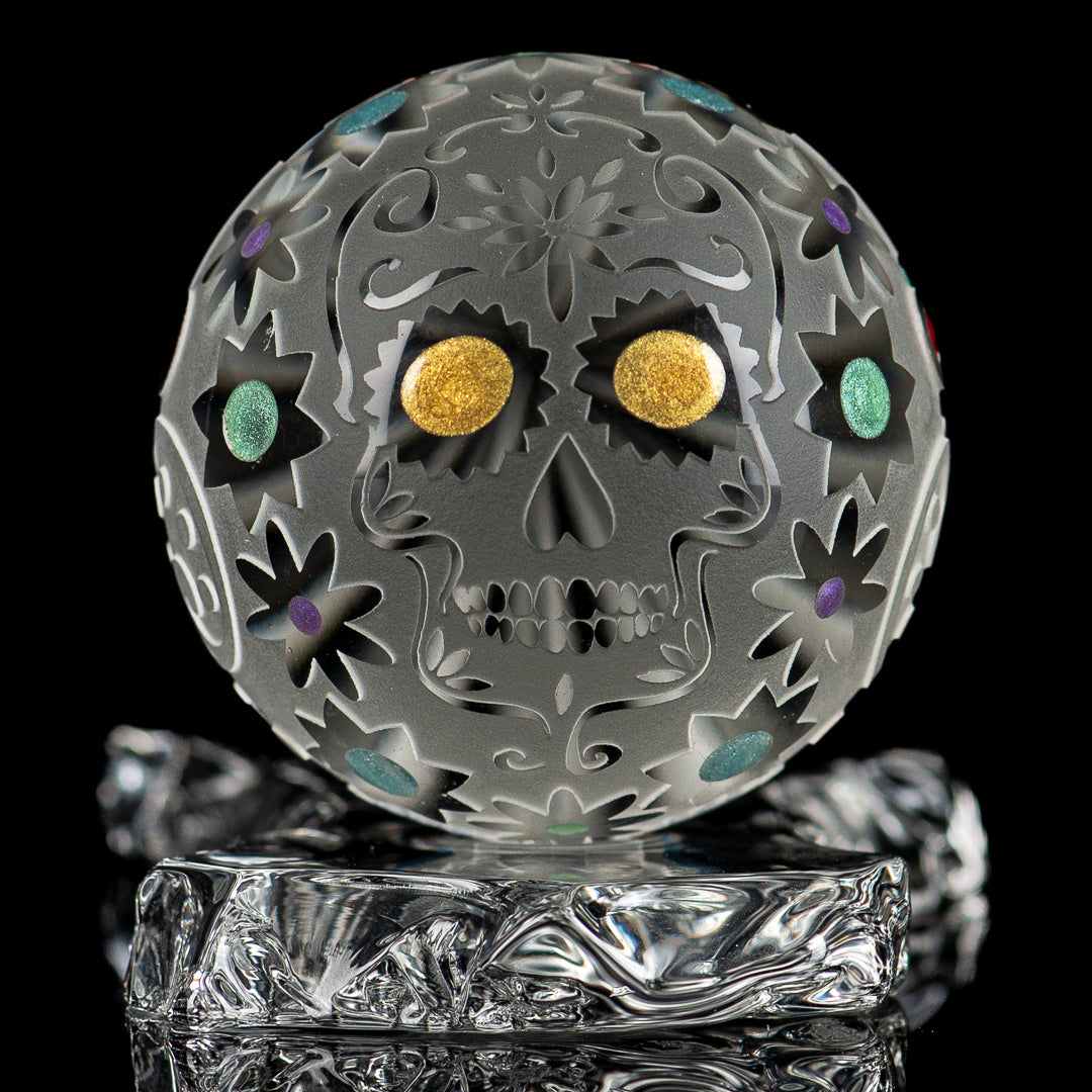 Faceted skull marble by Fatal Facets, made of glass with intricate faceted design, resting on a neutral surface.