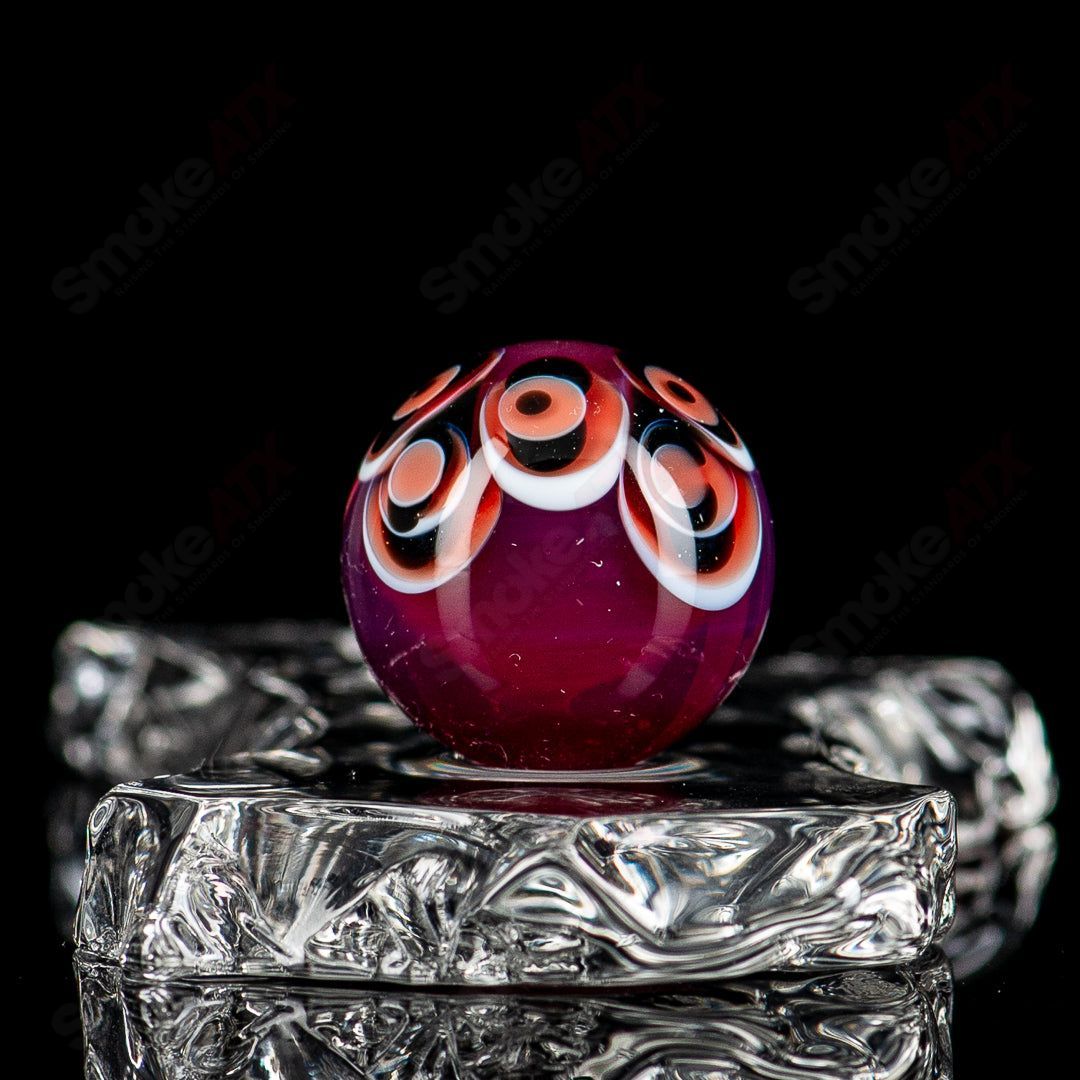 Red, black, and white dot stacked glass marbles by Indo Glass, showcasing colorful, patterned glass marbles on a neutral background.