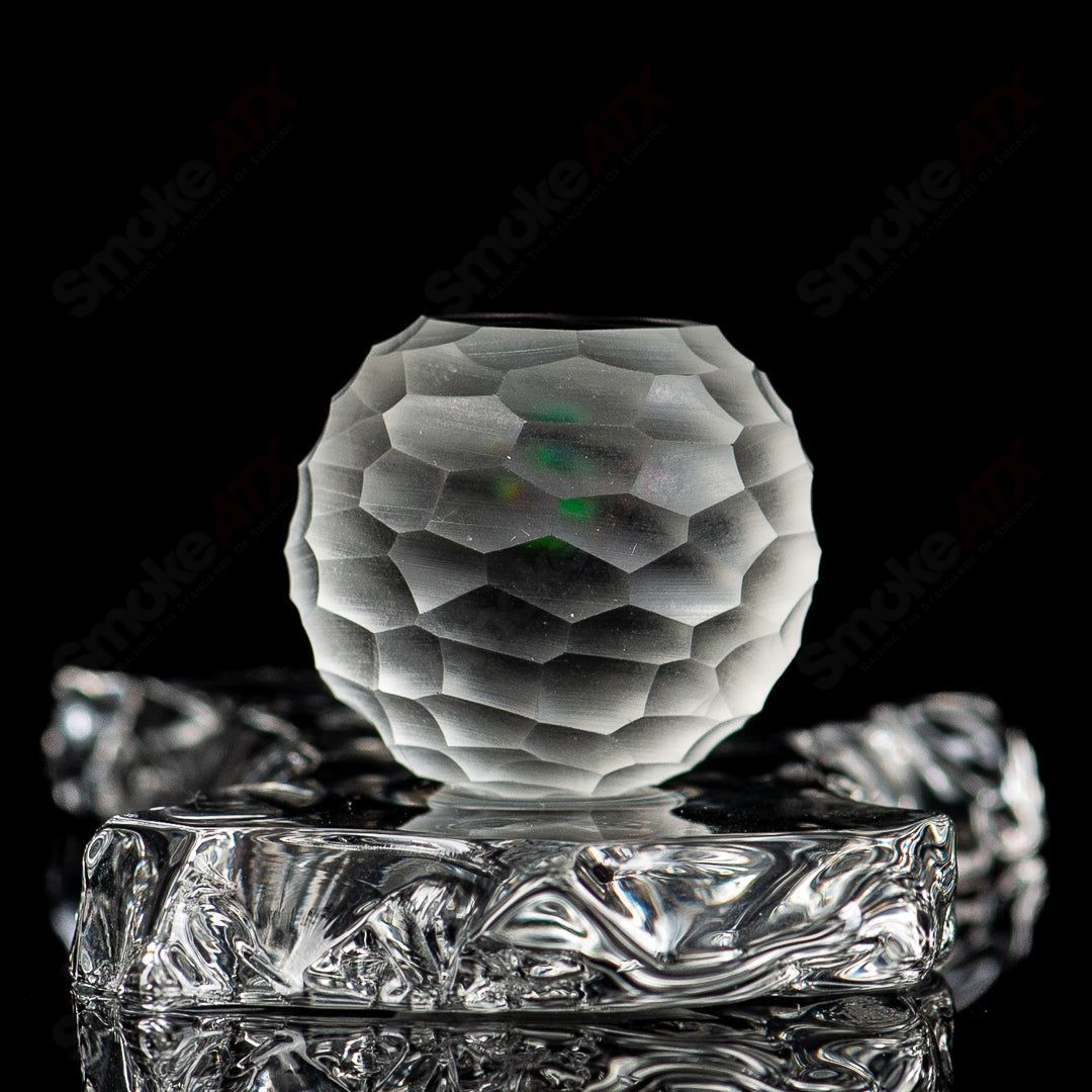 Faceted marble by Fatal Facets, a colorful glass marble with intricate faceted design on a white background.