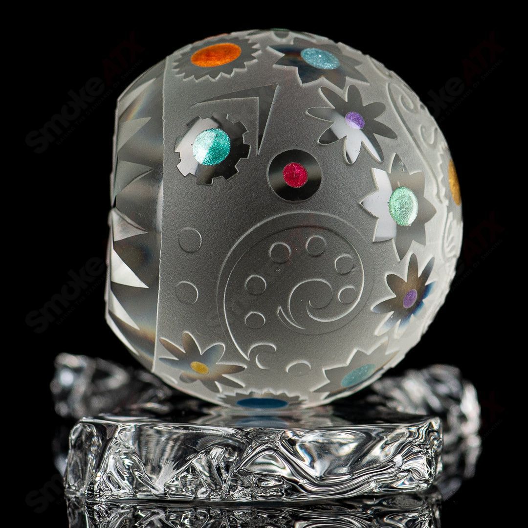 Faceted skull marble by Fatal Facets, a clear heady glass marble with intricate faceted design and skull shape on a reflective surface.